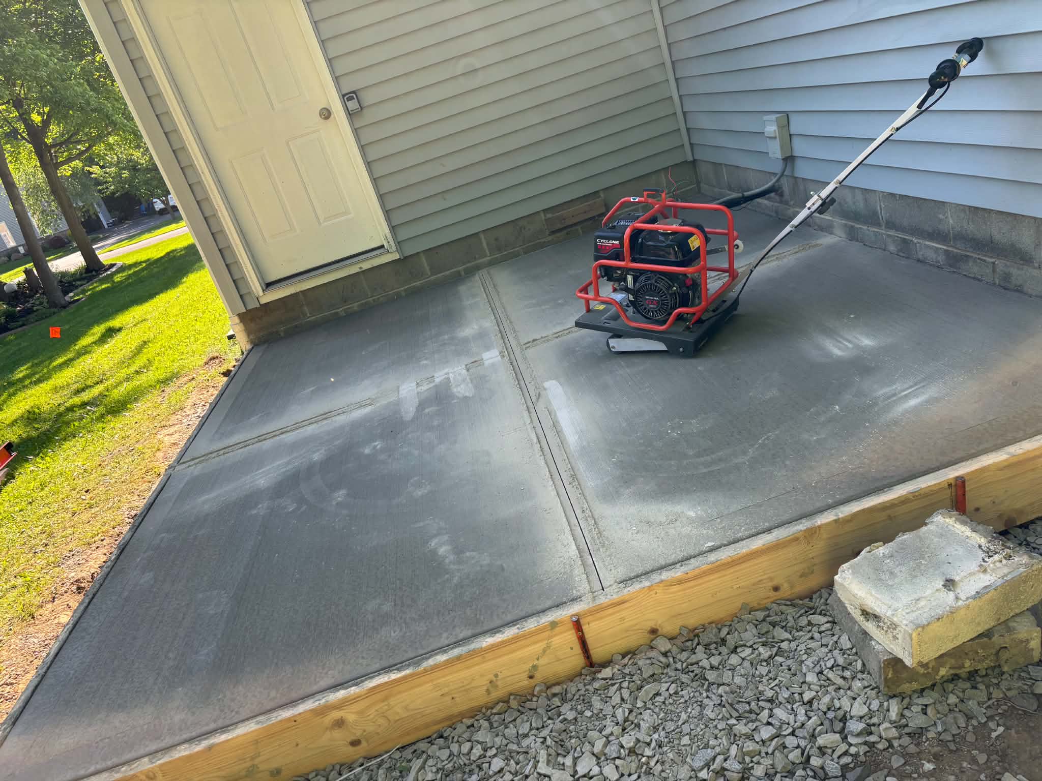 Keystone Masonry concrete patio installation Rochester NY — Cyclone power trowel finishing fresh slab with control joint visible