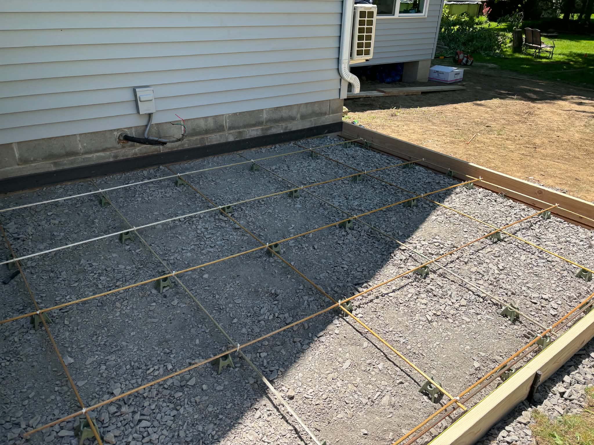 Rebar grid reinforcement prep for Keystone Masonry concrete patio installation Rochester NY — #4 rebar on chairs over compacted gravel base